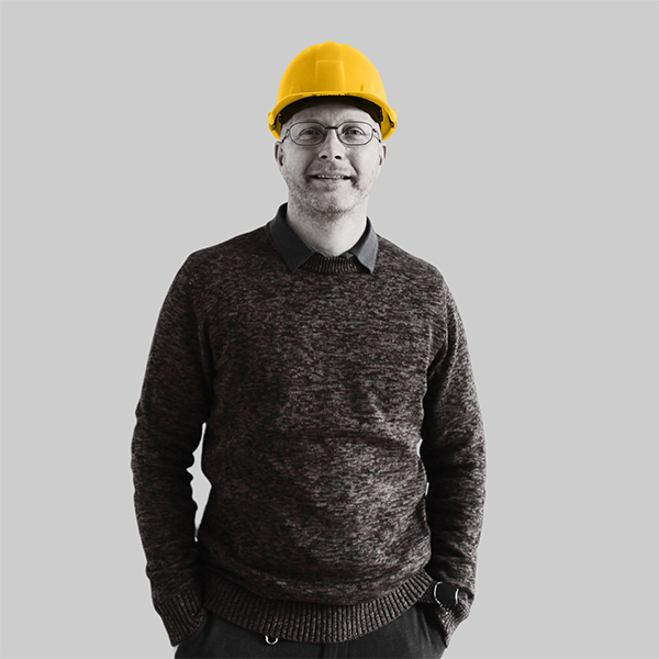 Team-rheform - Bernd di Flavio, M.A. Architekt von der Nachhaltigen Immobilienentwicklung Gebäudeanalyse hat einen Bauhelm auf und die Hände in den Taschen