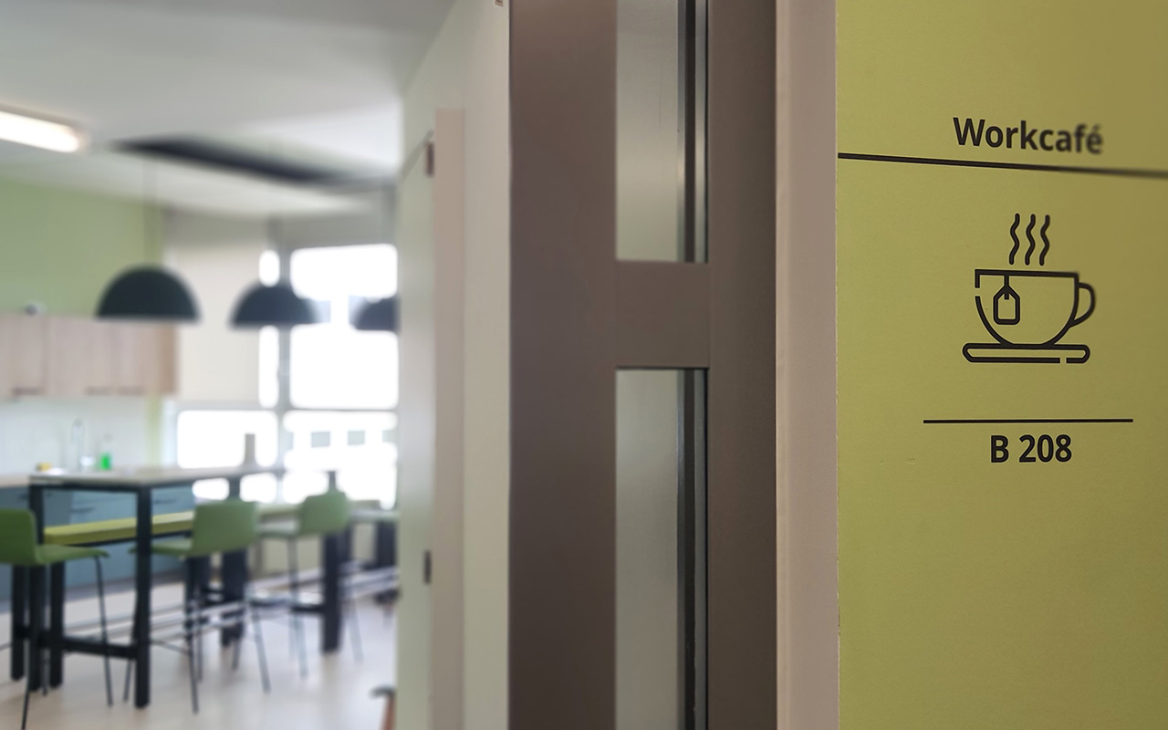 New-Work - Ein Icon auf grünem Hintergrund, der einen Raum für Kommunikation ausweist, führt die Mitarbeitenden der DB Cargo in München zum Work Café.