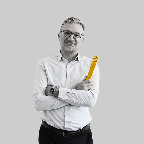 Team-rheform - Ivan Ivanov, Dipl. Ing. Architekt AKNW M.Sc. Real Estate Management, Prokurist und Bereichsleiter Zukunftsweisende Laborkonzepte und Nachhaltige Immobilienentwicklung Gebäudekonzepte hält einen zusammengeklappten Meterstab in der Hand und hat die Arme vor der BRust verschränkt