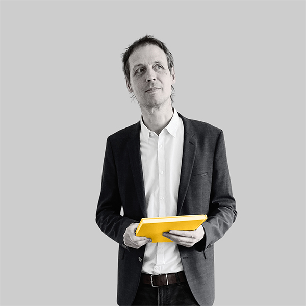 Team-rheform - Rochus Wiedemer, Dr. Ing. Architektur von der Zielorientierten Bedarfsplanung Projekt- und Kommunikationsmanagement hält ein Buch in beiden Händen und blickt nachdenklich in die rechte obere Ecke des Bildes