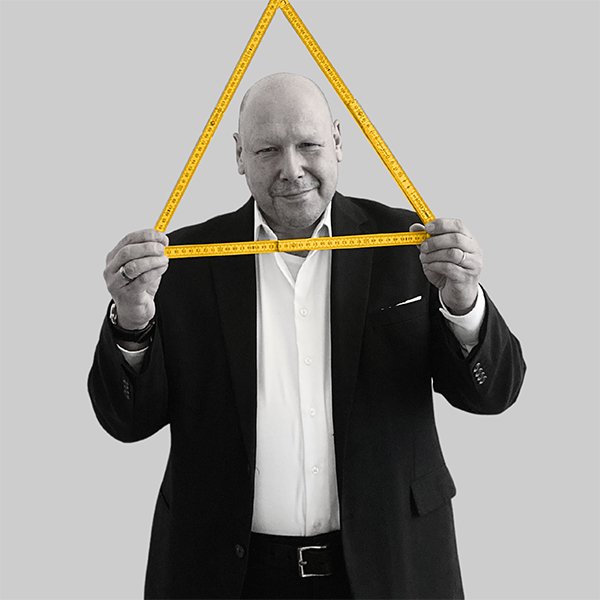 Team-rheform - Volker bocklenberg, Dipl. Ing. Architekt, Sachverständiger Schall- und Wärmeschutz hält einen zu einem Dreieck gefaltenen Meterstab auf Kopfhöhe. Er ist Teil der Nachhaltigen immobilienentwicklung Gebäudeanalyse.