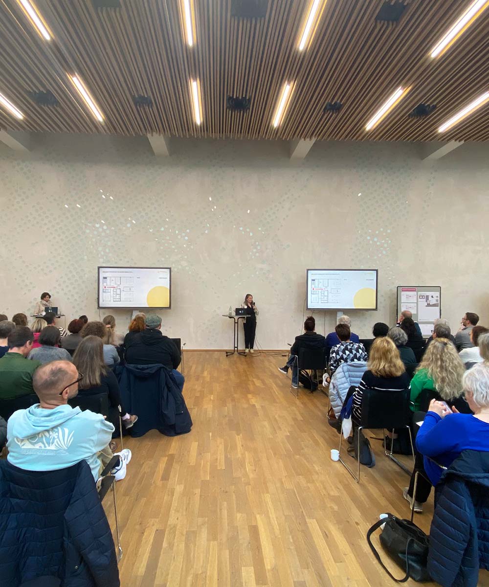 Transformationsbegleitung Wirkstatt evangelisch - Foto von Claudia Schirduan (rheform) bei der Townhall-Veranstaltung zwischen zwei Bildschirmen am Rednerpult.