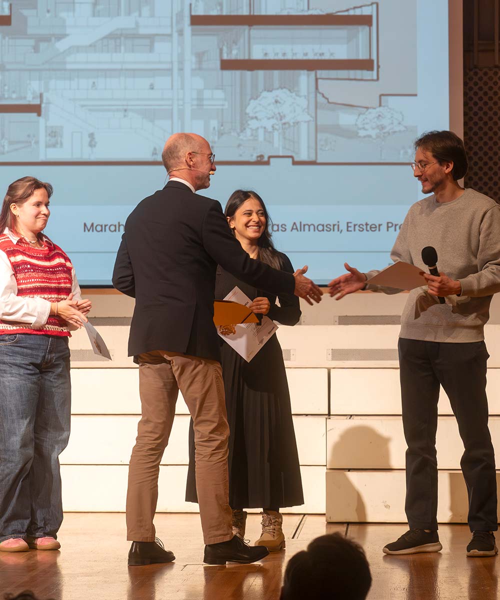 Preisverleihung-campus³-Preis-2025: Joachim Heintze überreicht den Gewinner:innen der sechsten Ausschreibungsrunde auf der Bühne des Bauwelt Kongresses ihre Urkunden.