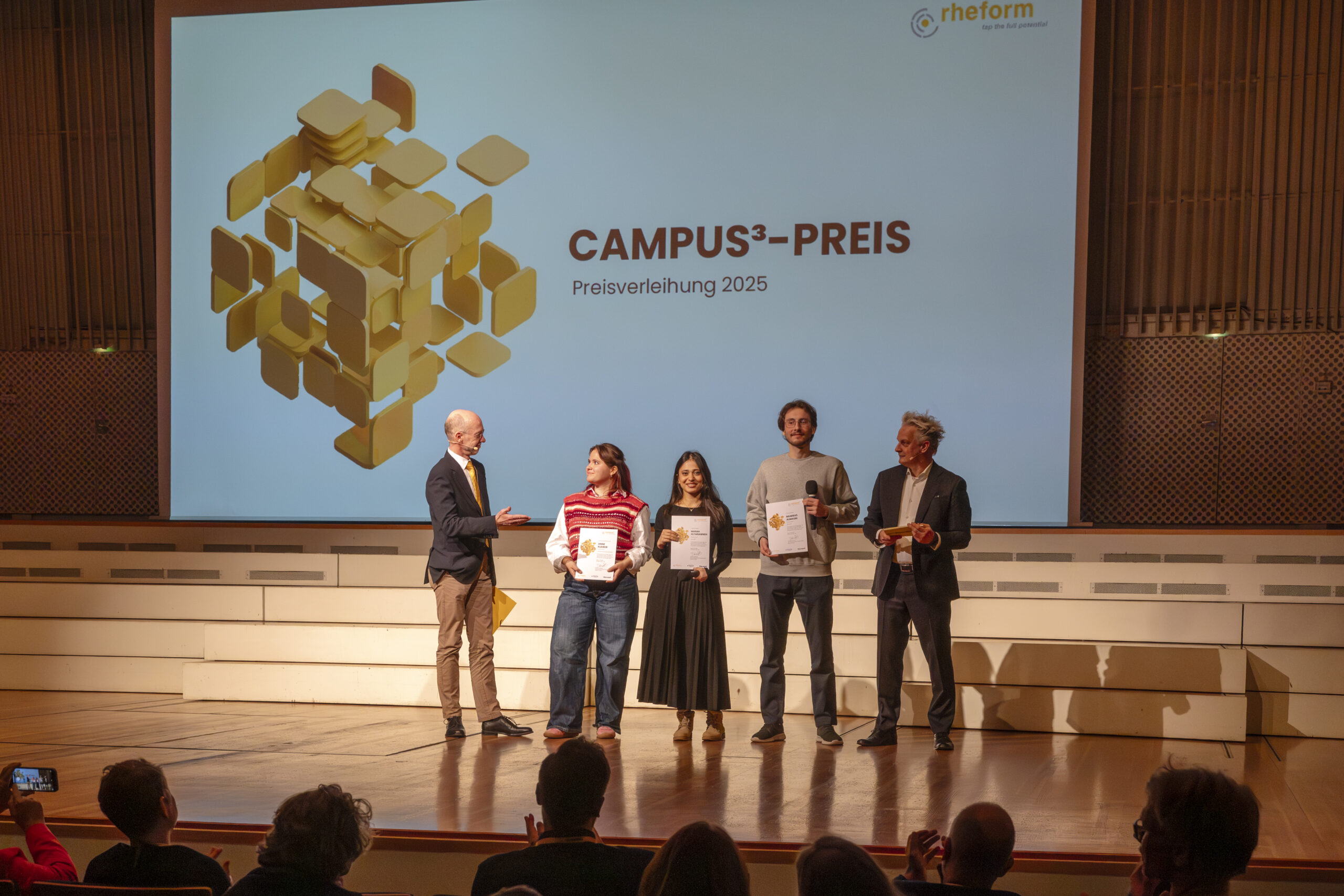 Zeigt die Gewinner:innen des campus³-Preises 2025 auf der Bühne mit Joachim Heintze von der rheform und Boris Schade-Bünsow von der Bauwelt.